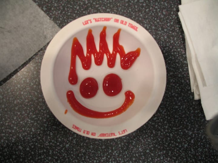 a smiling face drawn out of ketchup on a plate